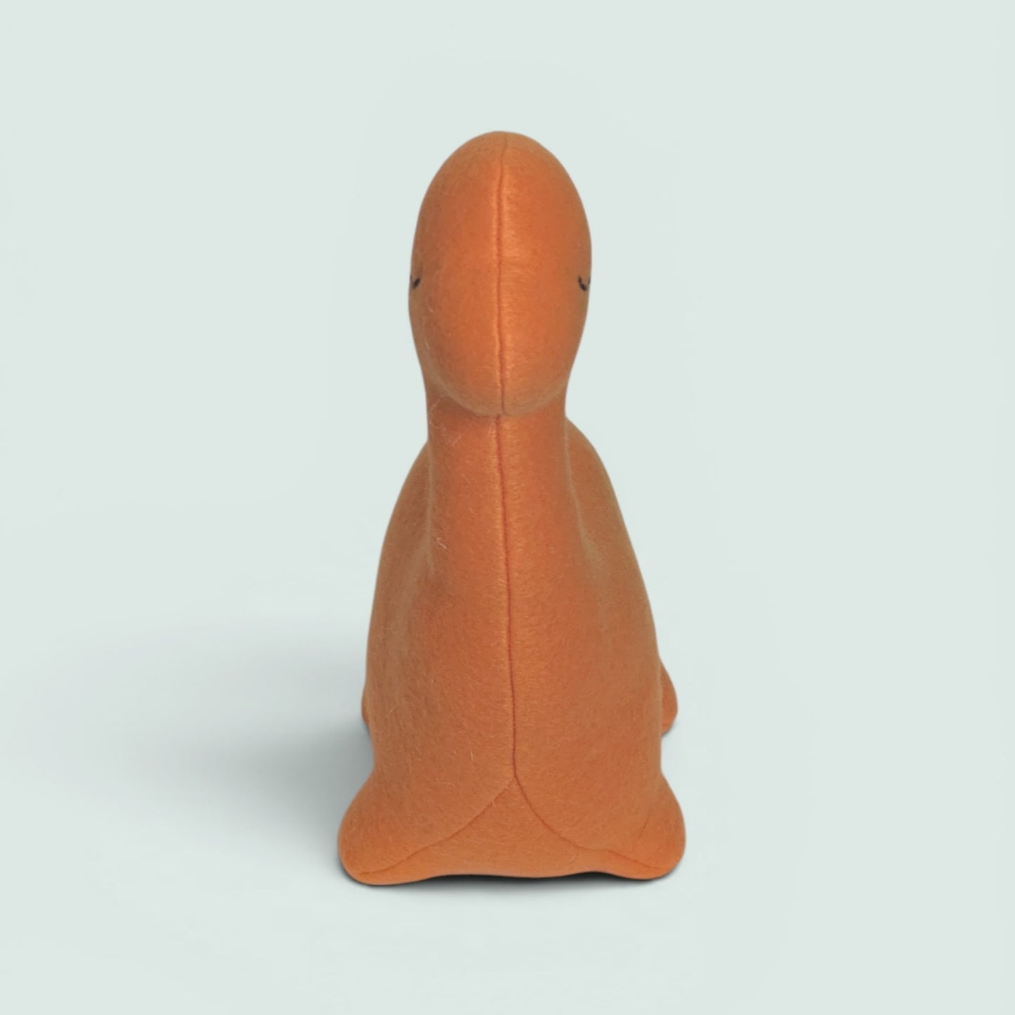 An orange plush dinosaur toy with embroidered eyes, shown from the front against a light gray background.