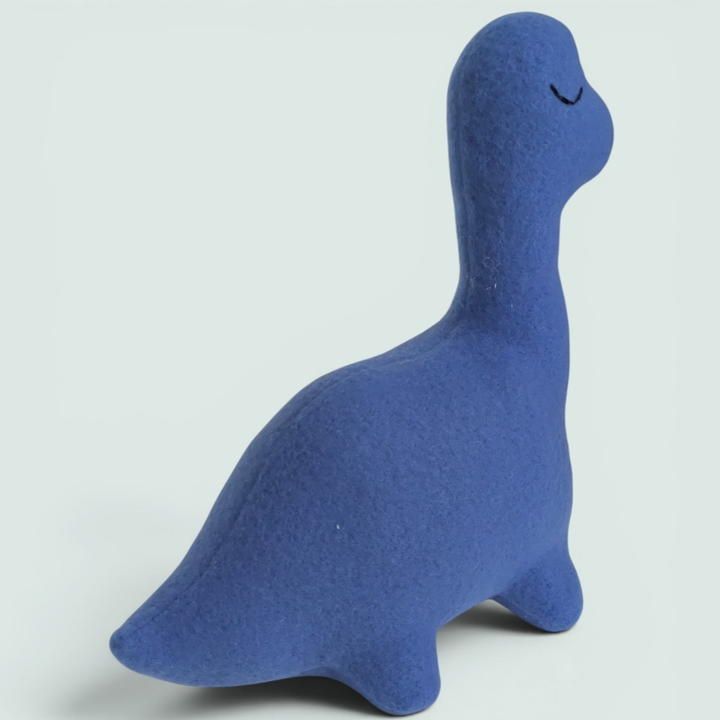 A blue fleece dinosaur toy with a long neck and closed eyes, photographed on a light gray background.