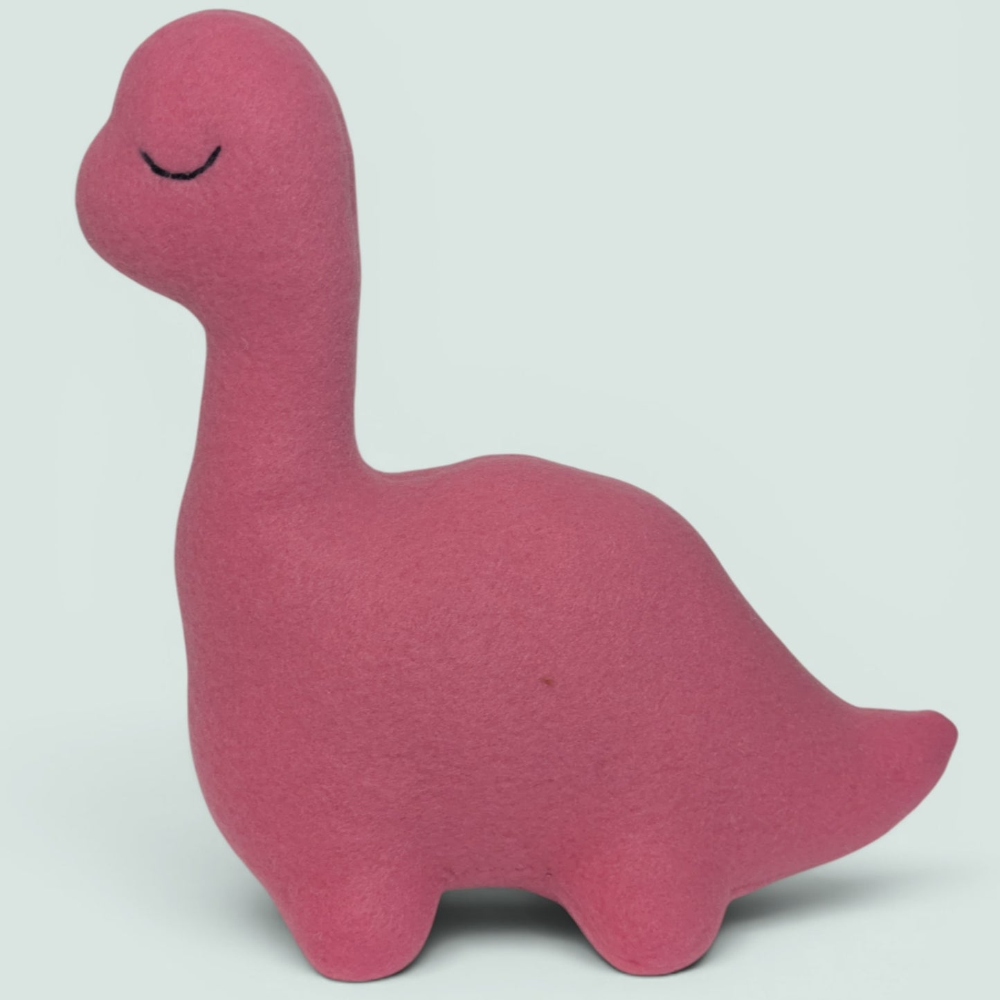 A pink fleece dinosaur toy with a long neck and embroidered closed eyes, shown against a plain light gray background.