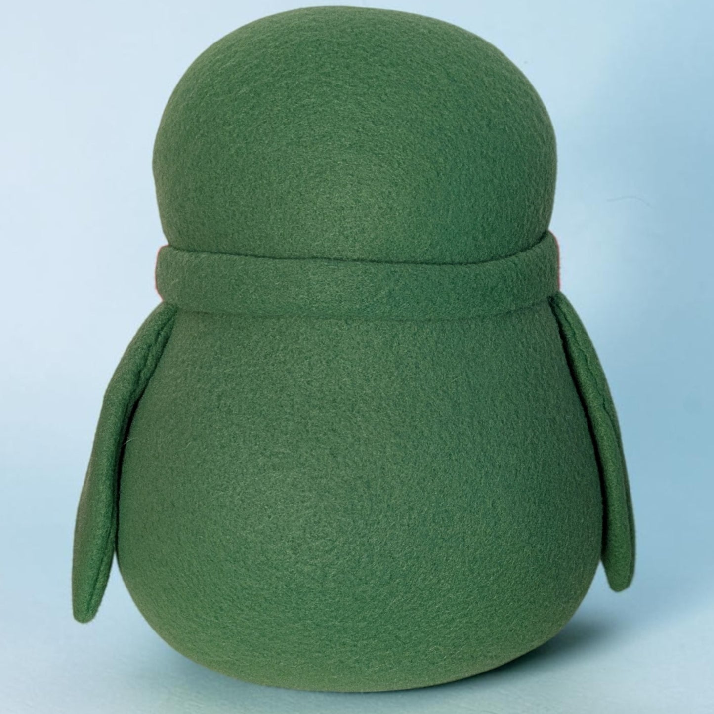 A green fleece penguin stuffed animal with a rounded body, wings, and a matching scarf, shown against a light blue background.