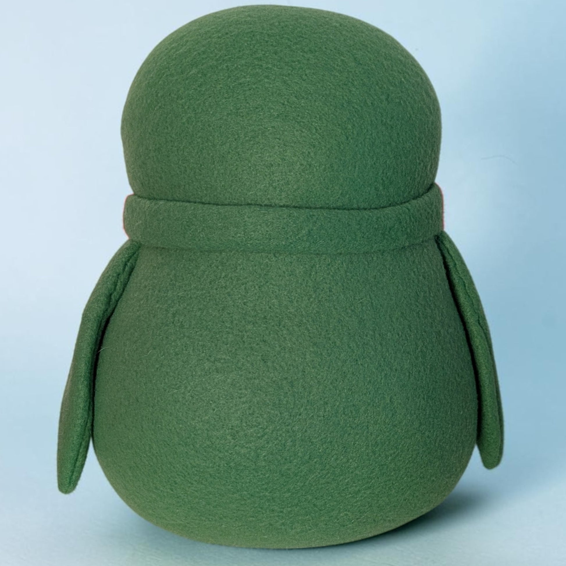 A green fleece penguin stuffed animal with a rounded body, wings, and a matching scarf, shown against a light blue background.