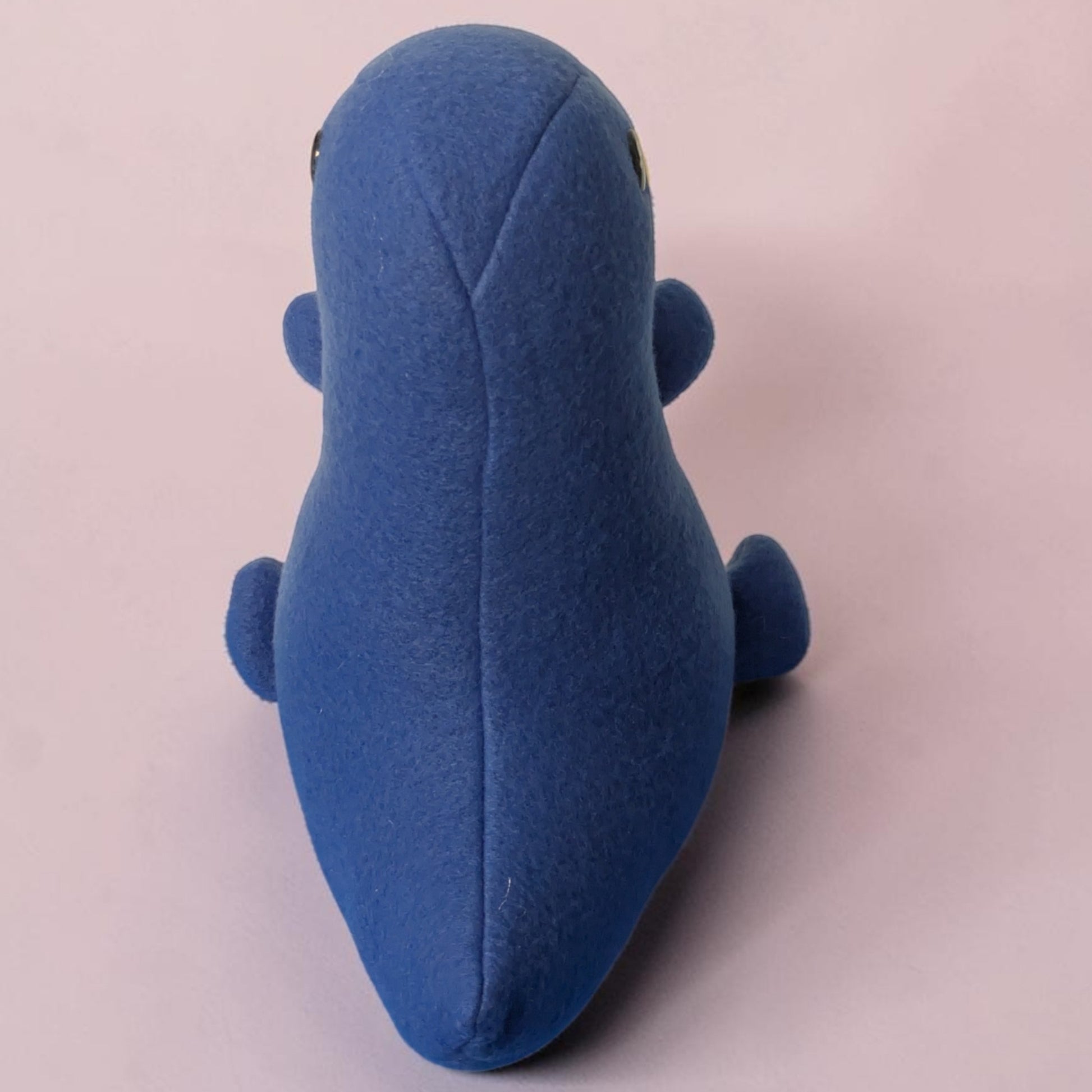 A blue plush toy shaped like a dinosaur, photographed from the back against a solid pale pink background.