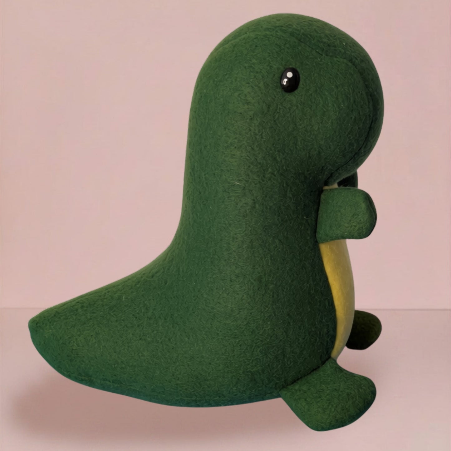 A green fleece dinosaur plush toy with a yellow belly and small black eyes, shown against a soft pink background.