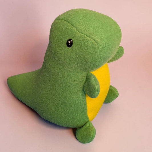 A green fleece dinosaur plush toy with a yellow belly and a small black safety eye, sitting on a soft pink background.
