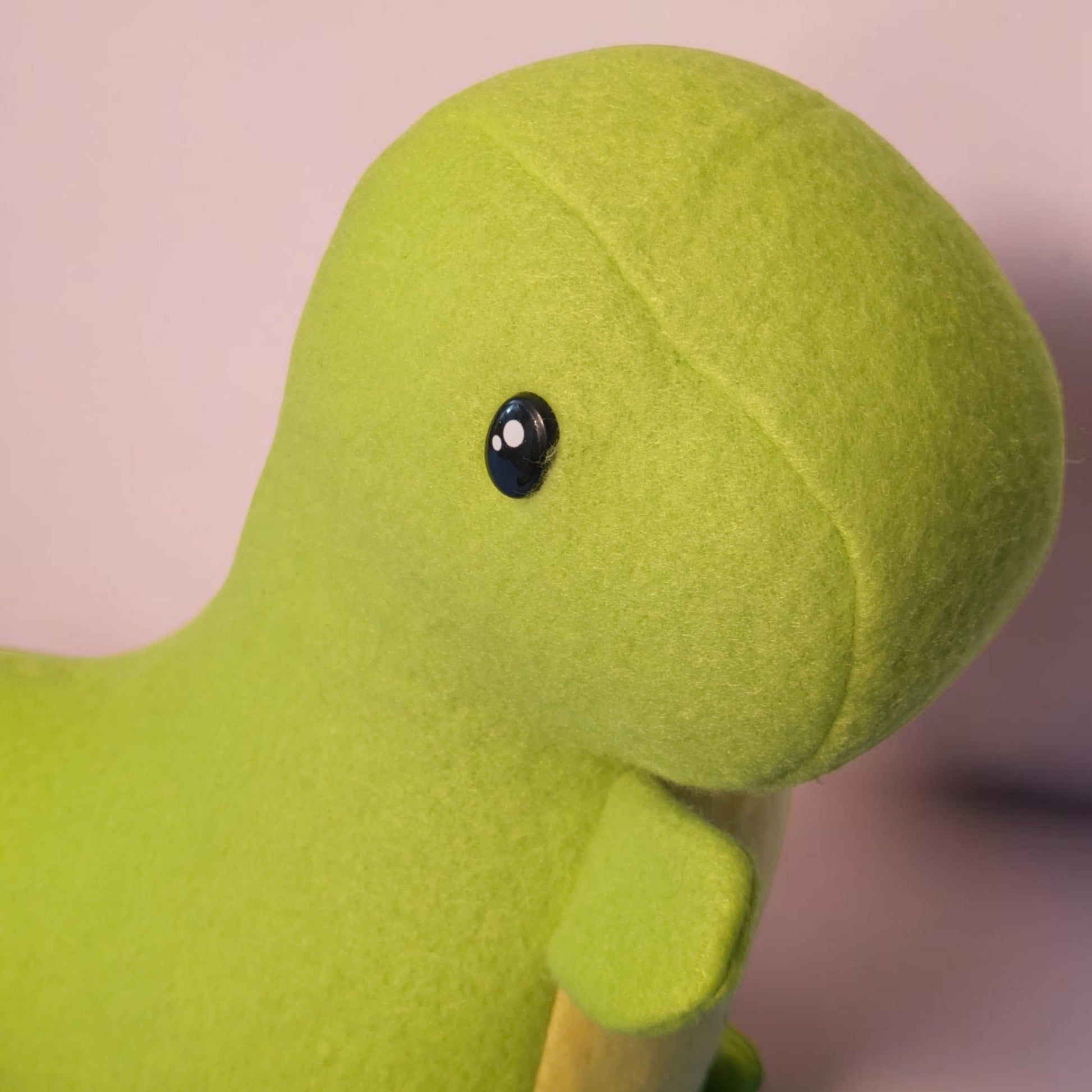 A close-up of a bright lime green fleece dinosaur toy with a glossy black eye and a yellow belly