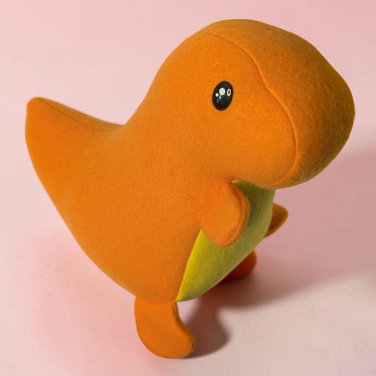 An orange plush dinosaur toy with a small yellow belly patch and black safety eyes, standing on a soft pink background.