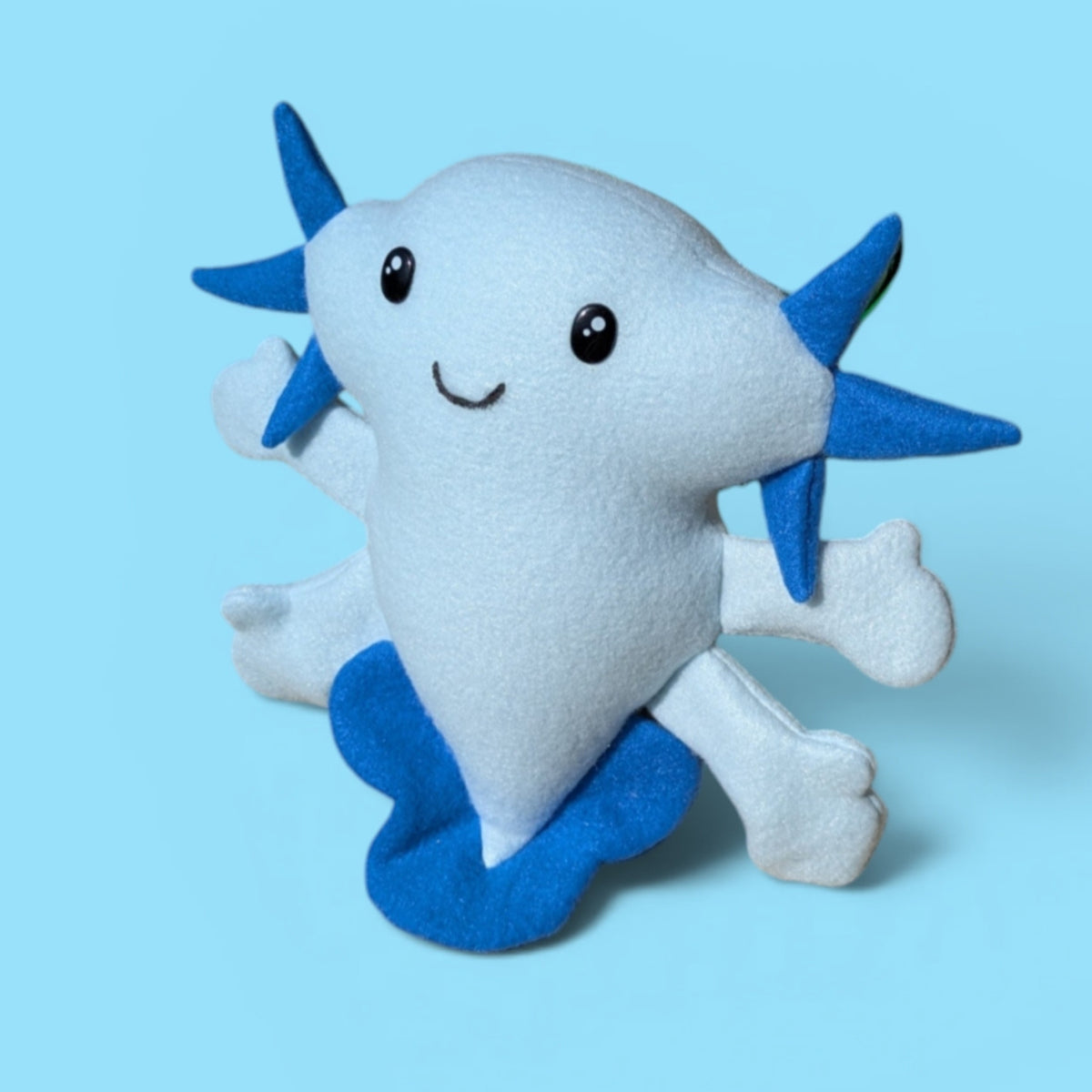 A cute, plush toy axolotl in light blue and dark blue fleece, set against a solid light blue background.
