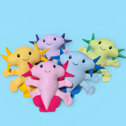 Five colorful plush axolotl toys arranged together on a light blue background. The toys are made of soft fleece fabric and have happy facial features.