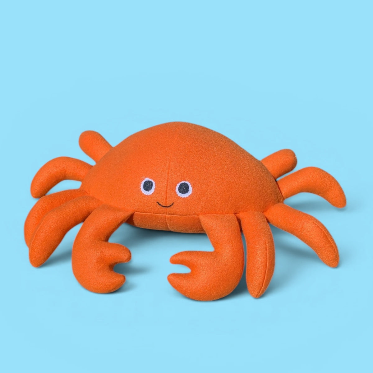 An orange plush crab toy with felt eyes and a smile, set against a solid light blue background.