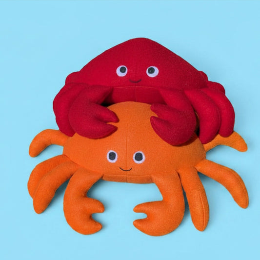 Two plush toy crabs, with a smaller orange crab underneath and a larger red crab sitting on top, set against a solid light blue background.