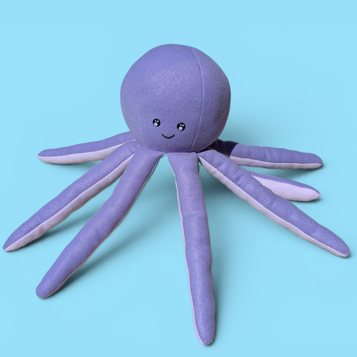 A purple plush octopus toy with a smiling face, photographed on a solid light blue background.