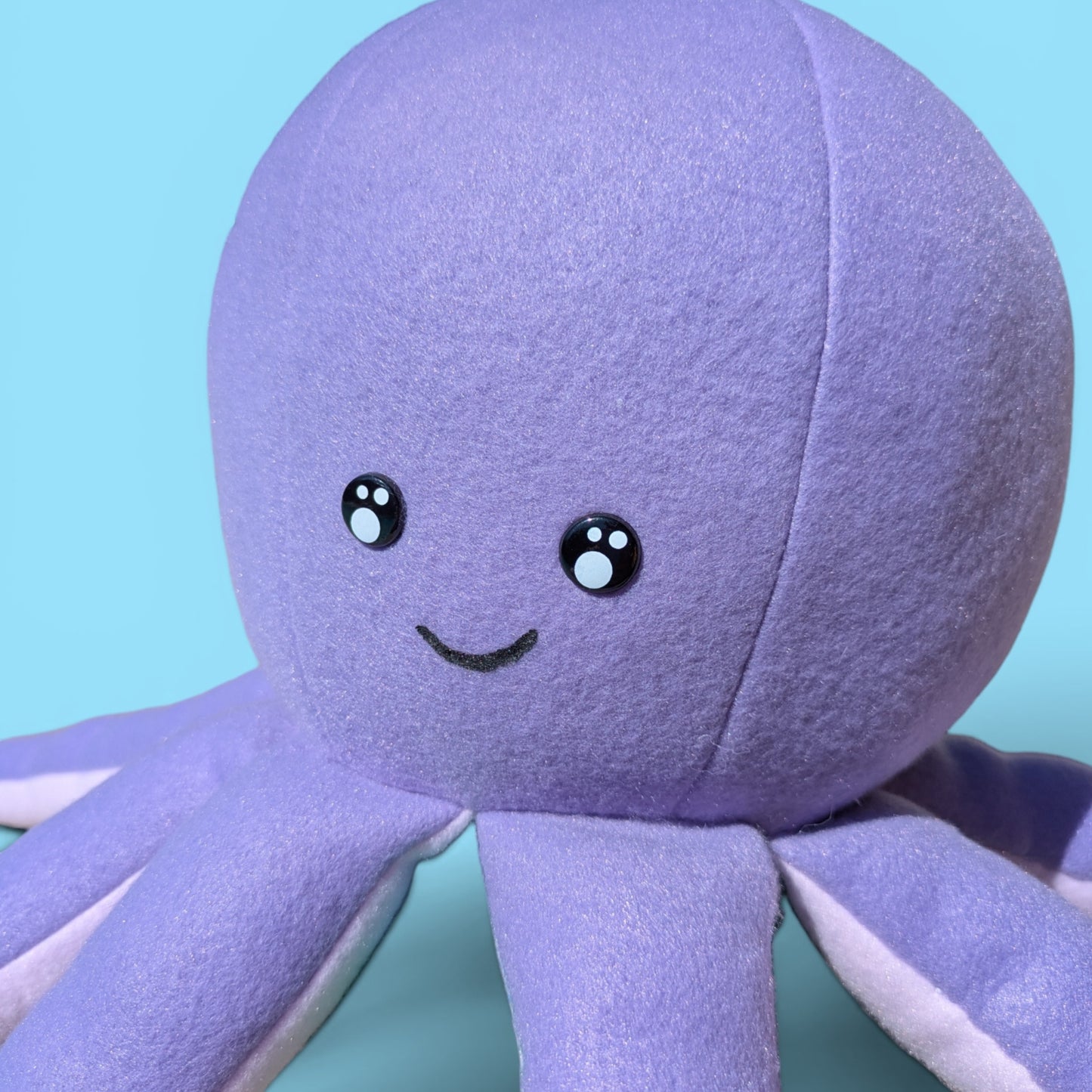 Close up of a purple plush octopus stuffed animal with a smiling face and kawaii eyes