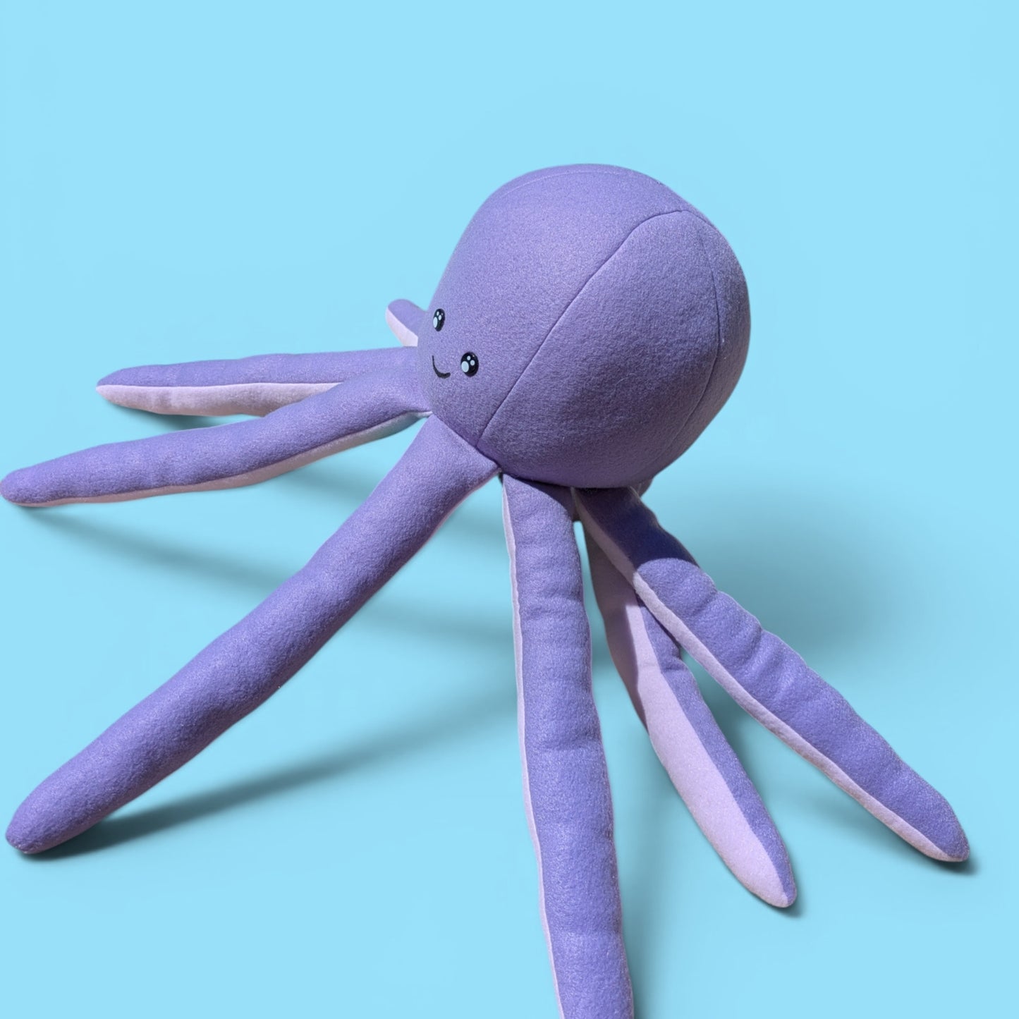 A purple octopus plush toy with a smiling face, photographed on a solid light blue background.