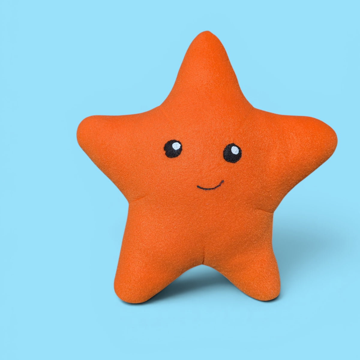 An orange starfish-shaped plush stuffed animal with a cute smiley face, set against a solid light blue background.