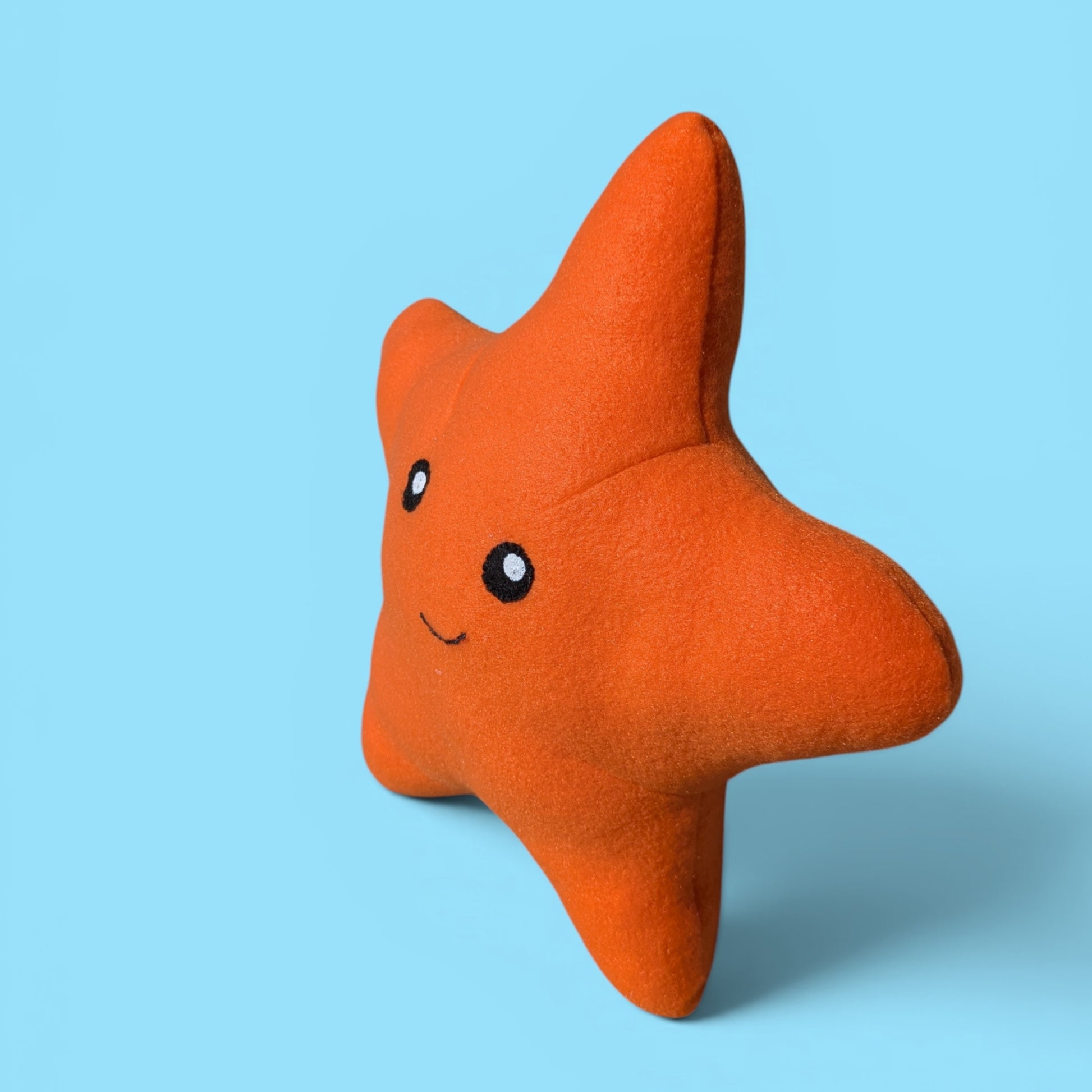 An orange starfish-shaped plush toy with felt eyes and a smile, standing on a light blue background.