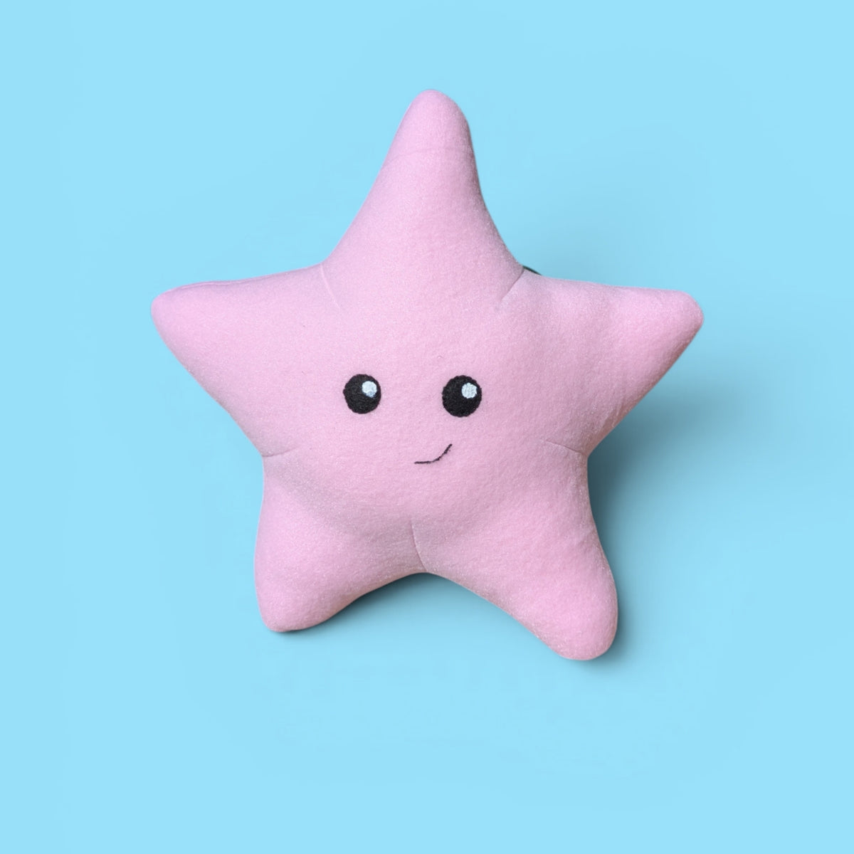 A pink star-shaped plush stuffed animal with a cute felt face, set against a solid light blue background.