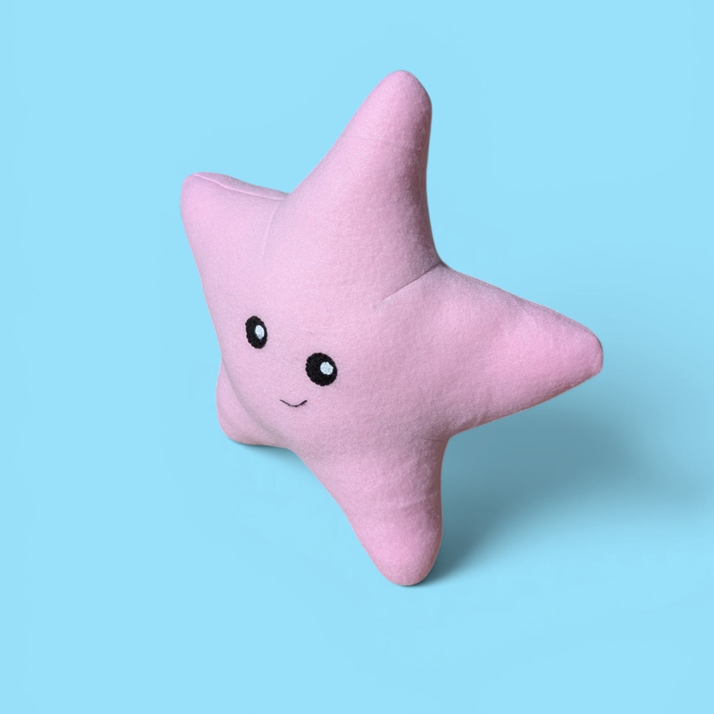 A pink star-shaped plush stuffed animal with a cute embroidered face, set against a solid light blue background.