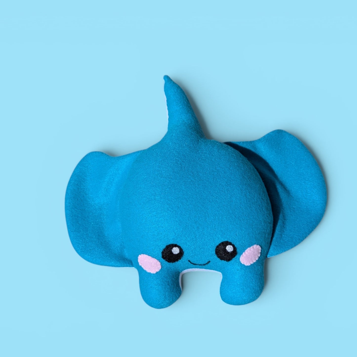A blue fleece stingray plush toy with stitched on black eyes, a small smile, and pink cheek details, centered on a light blue background.