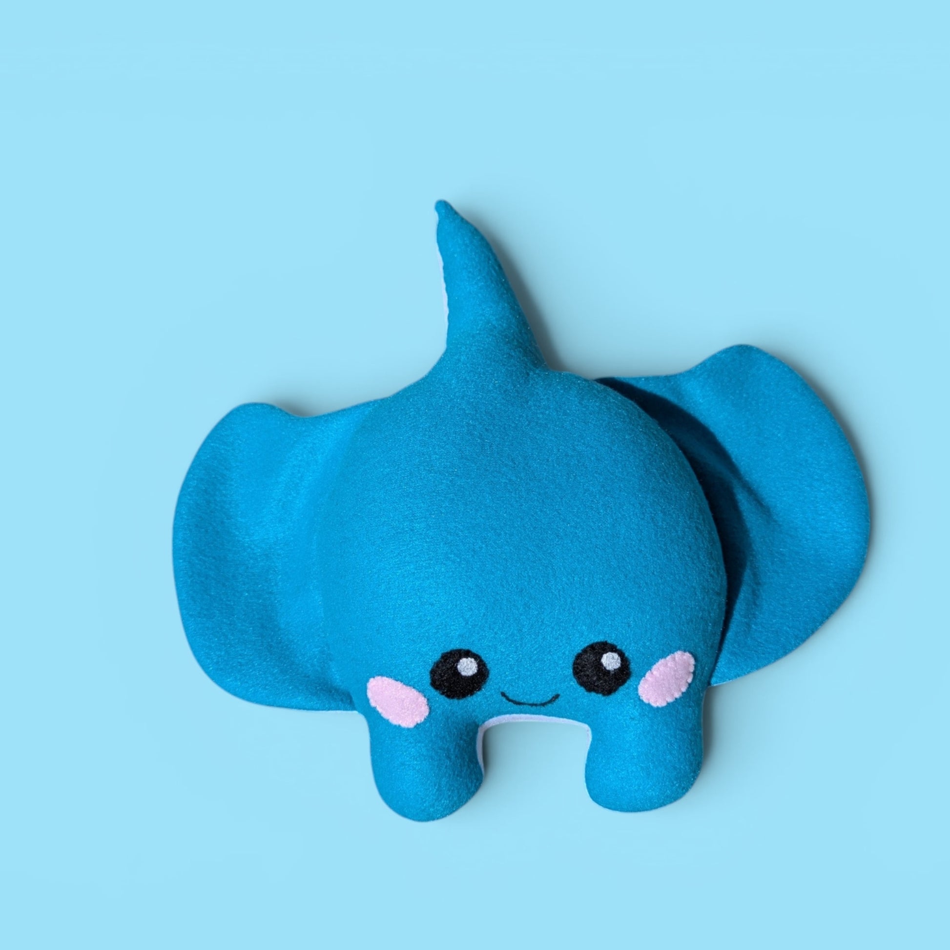 A blue fleece stingray plush toy with stitched on black eyes, a small smile, and pink cheek details, centered on a light blue background.