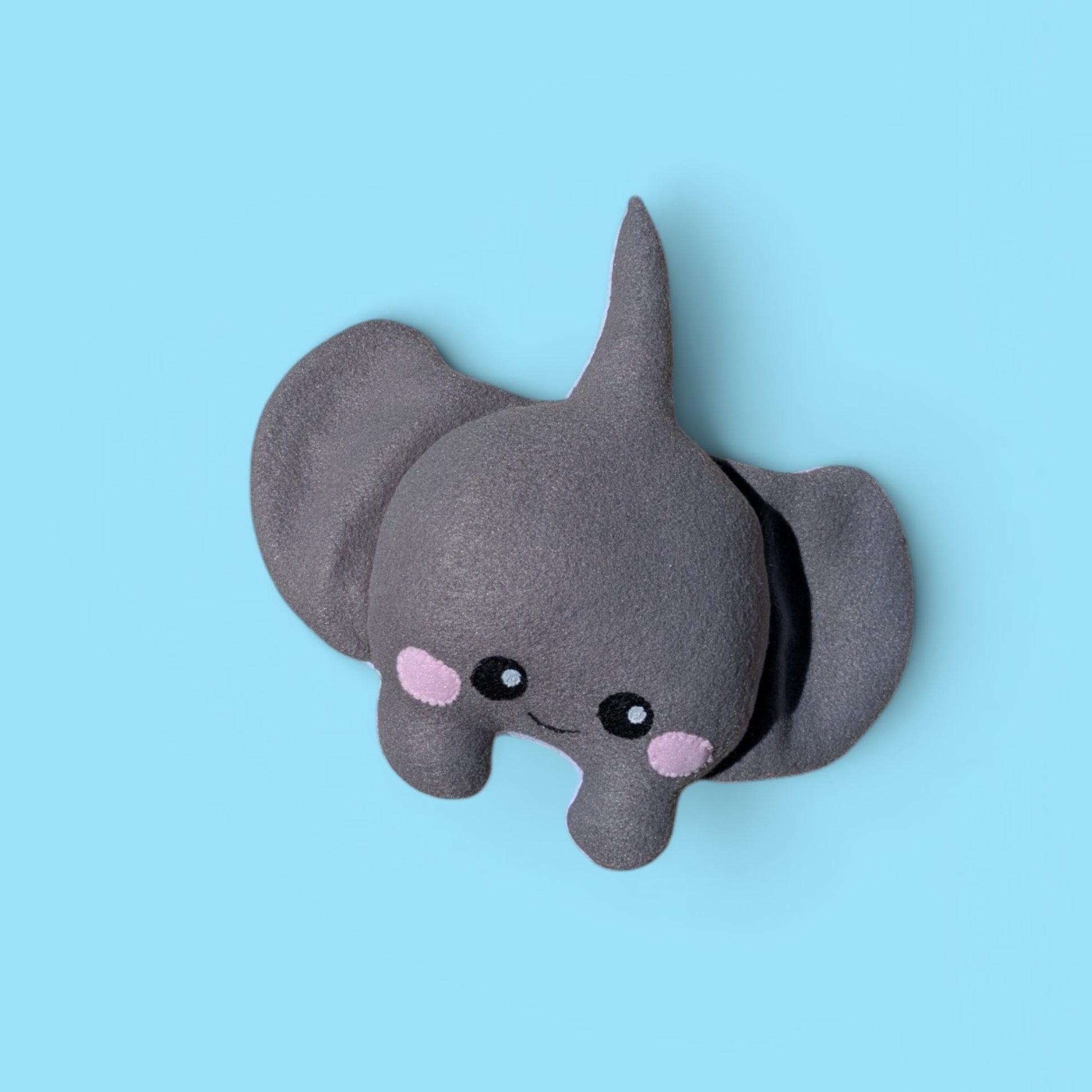 A small plush stingray toy in dark gray with pink cheeks and black felt eyes, photographed against a solid light blue background.