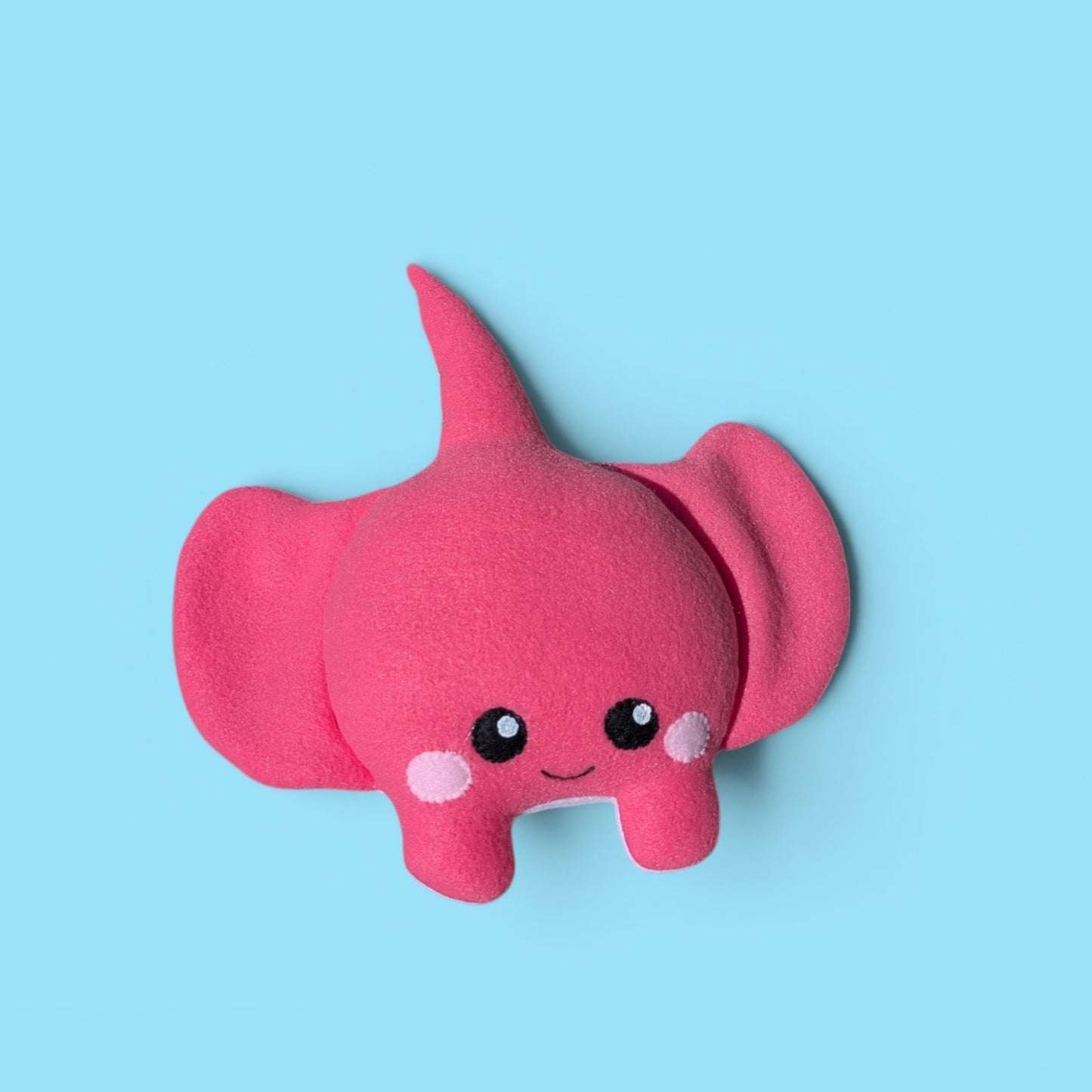 A pink fleece stingray plush toy with a cute felt face, set against a solid light blue background.
