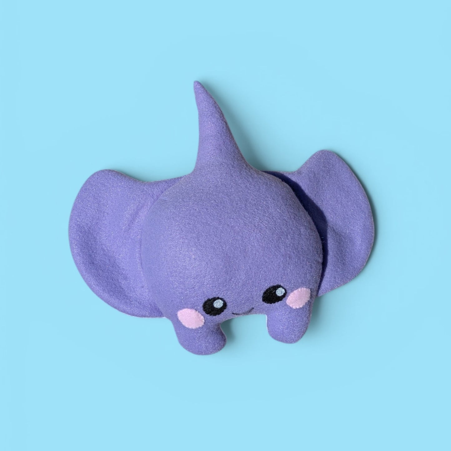 A cute purple felt stingray plush toy with large floppy fins, small black eyes, and pink cheeks, shown on a solid light blue background.