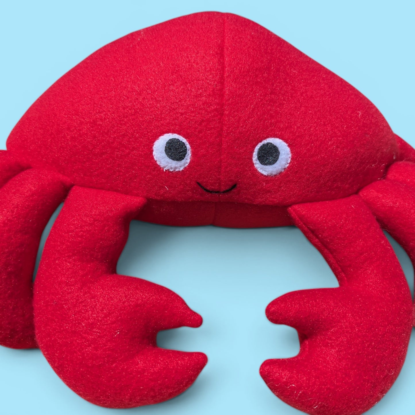 Close up of a red fleece plush crab stuffed animal face with sewn felt eyes and a small smile.