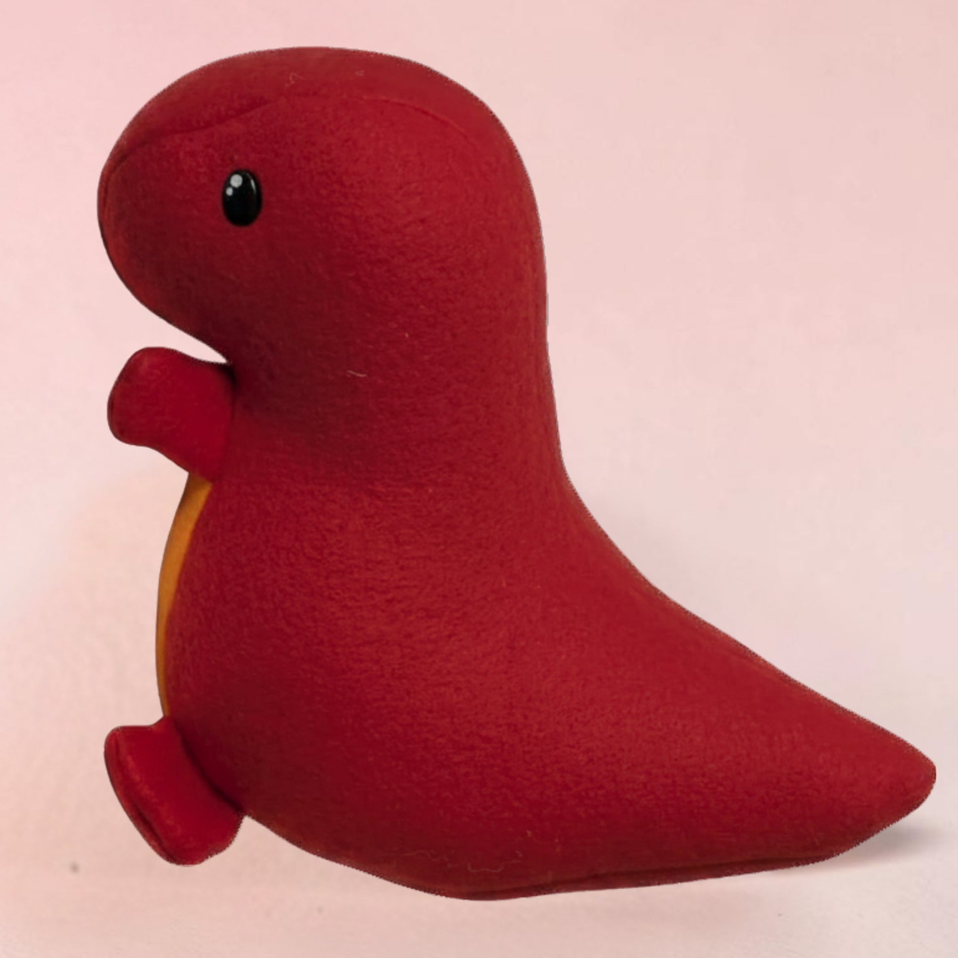 A handmade fleece  red plush dinosaur stuffed animal toy with a small black eye and a orange belly, photographed against a solid pale pink background.