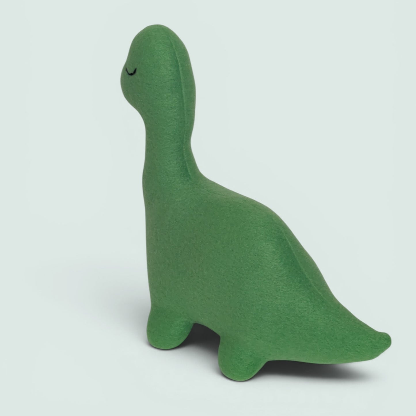 A green fleece dinosaur-shaped plush toy with a black embroidered eye, sitting against a solid light blue background.