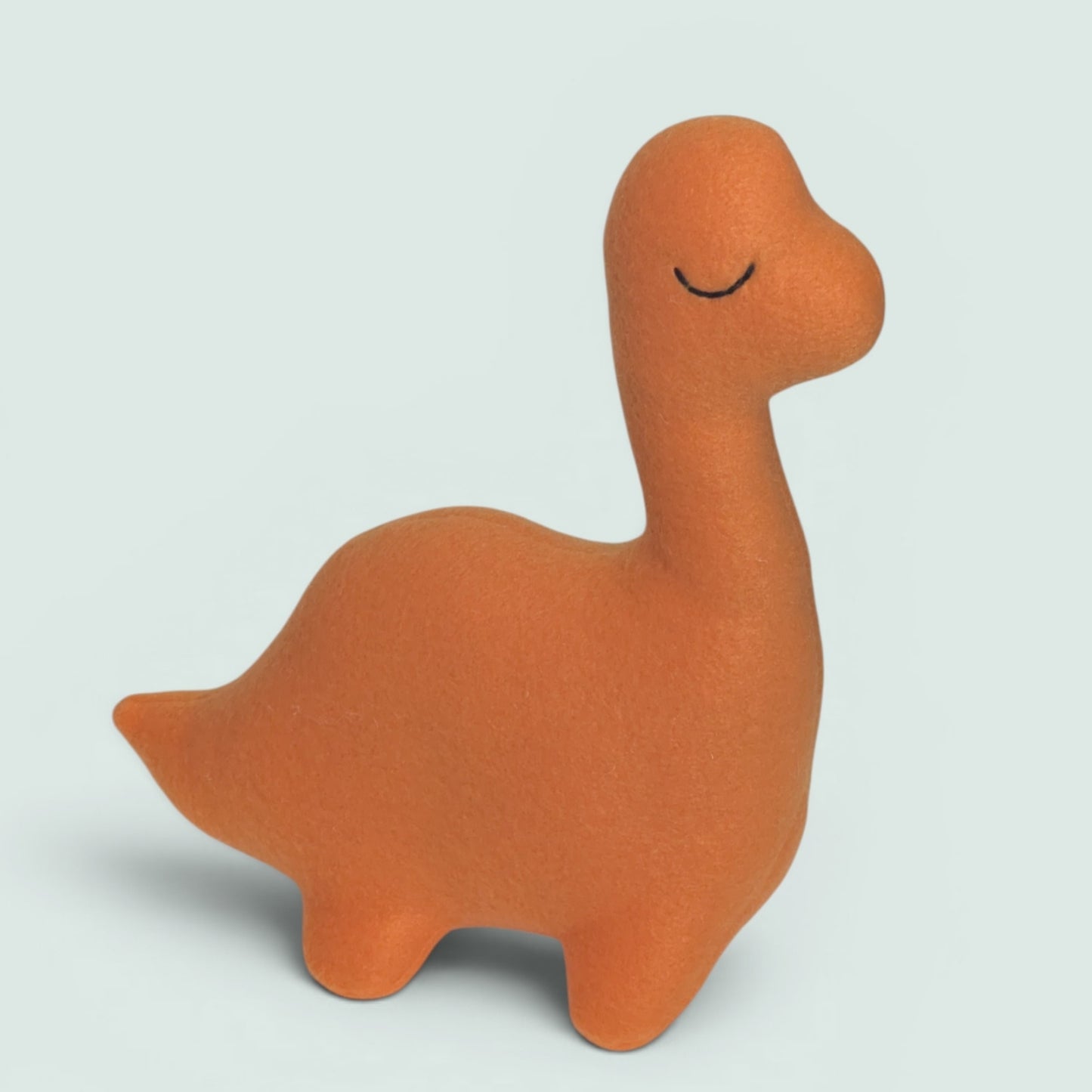 An orange fleece dinosaur toy with a closed smiling eye, standing on a light gray background.