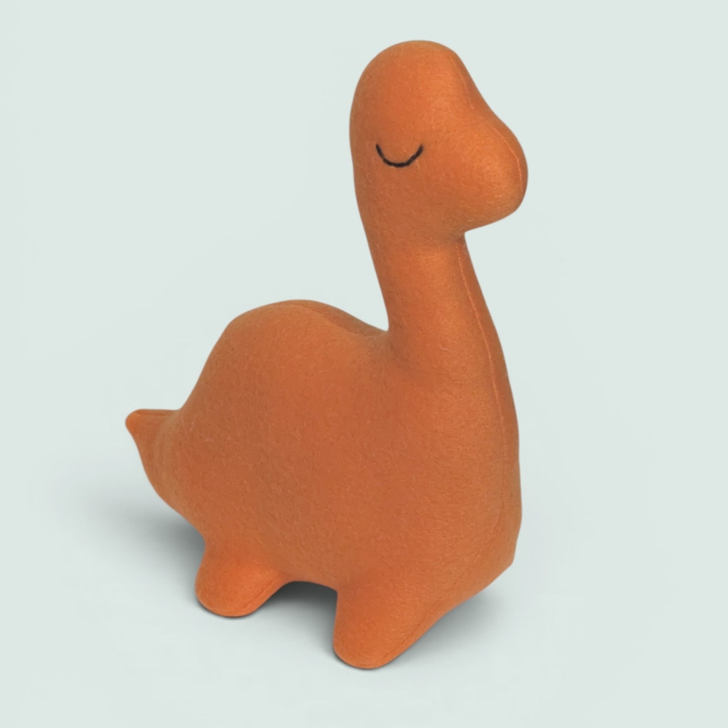An orange fleece dinosaur toy with a simple black stitched smile, shown on a light gray background.