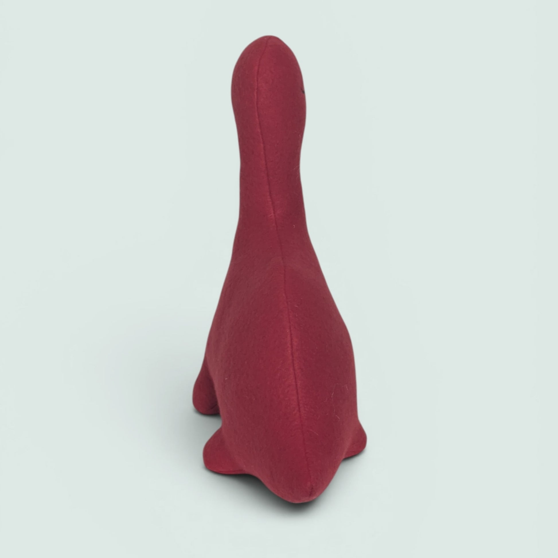 A red plush dinosaur toy shown from the back against a light gray background.