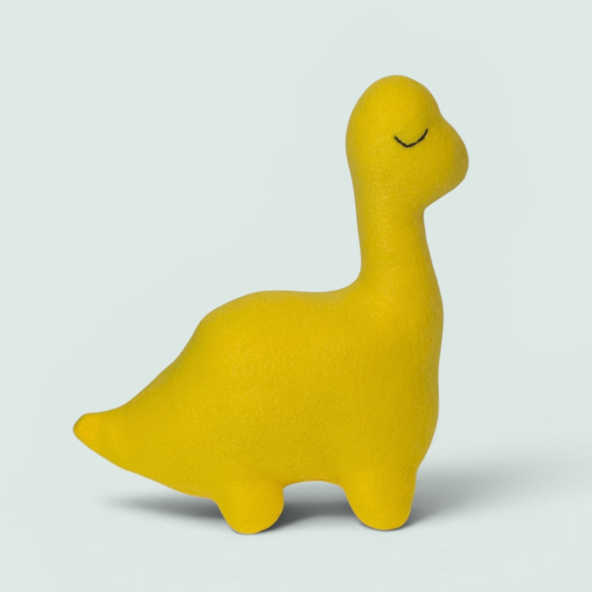 A bright yellow dinosaur toy with a long neck and closed eyes, standing on a light gray background.