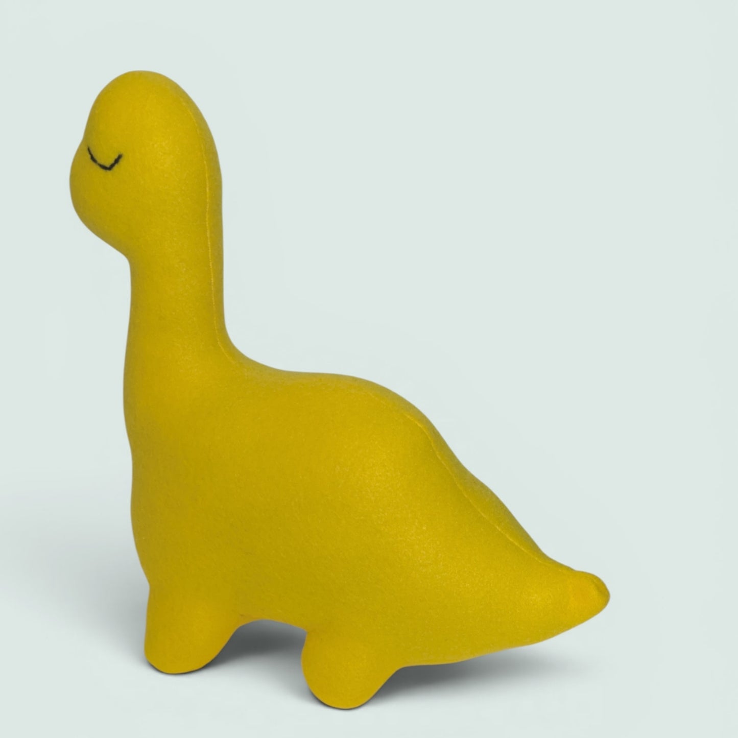 A bright yellow dinosaur-shaped plush toy with a sleeping face, shown on a light gray background.