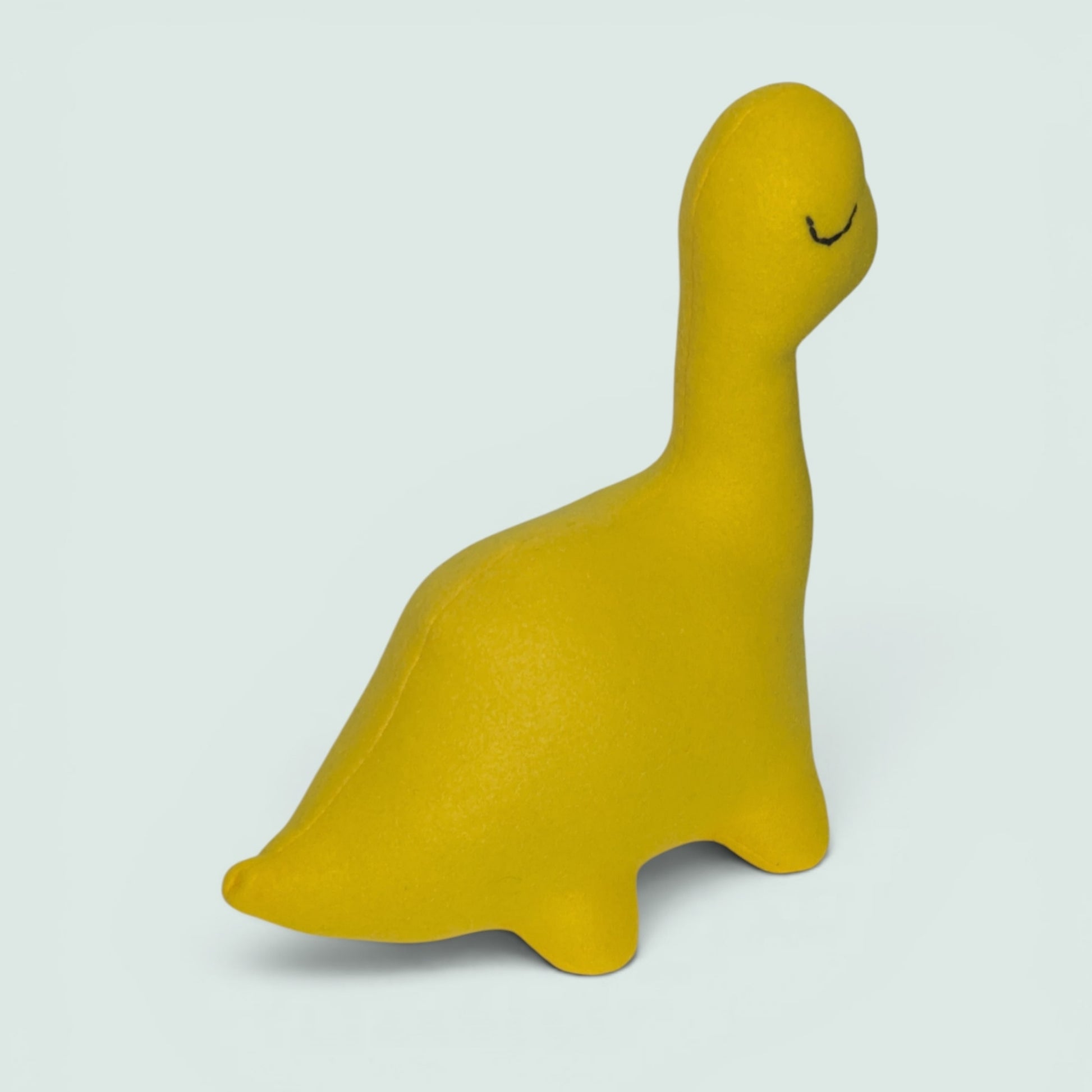 A yellow plush dinosaur toy with a black stitch eye, photographed against a soft blue background.