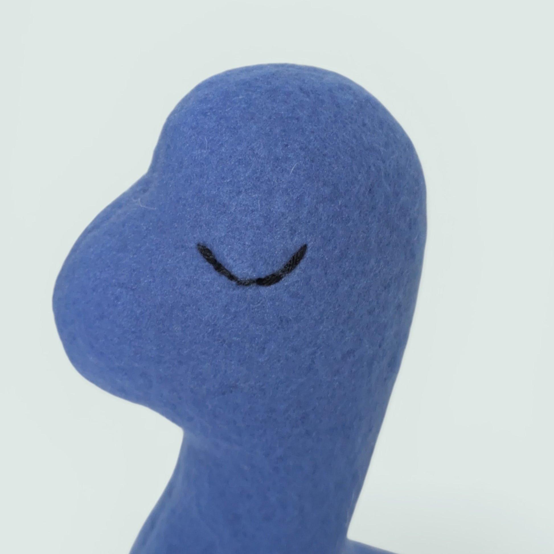 A close-up side profile of a blue fleece plush dinosaur toy with a simple black embroidered eye, set against a plain light gray background.