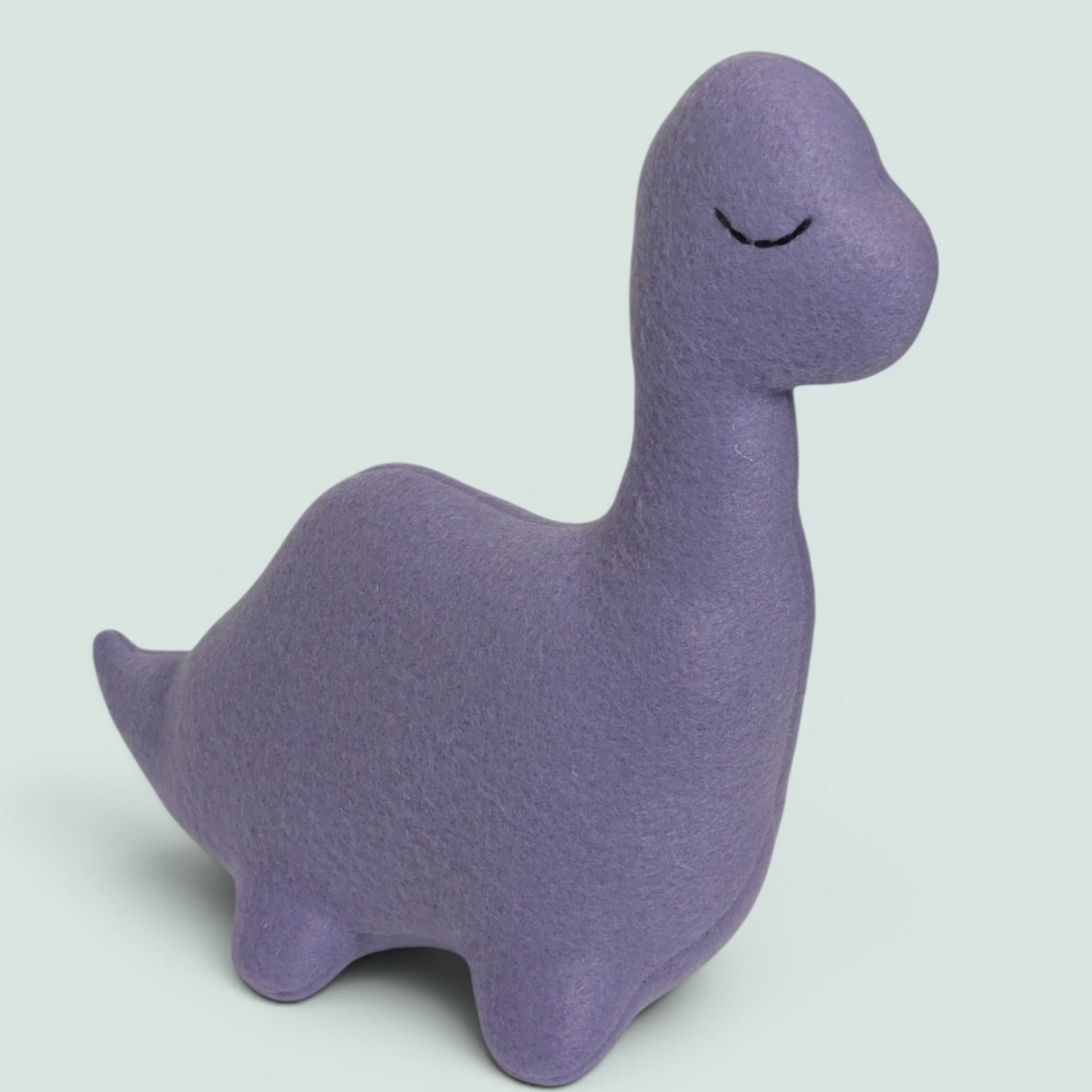 A light purple plush toy shaped like a dinosaur, photographed from the back against a solid pale green background.