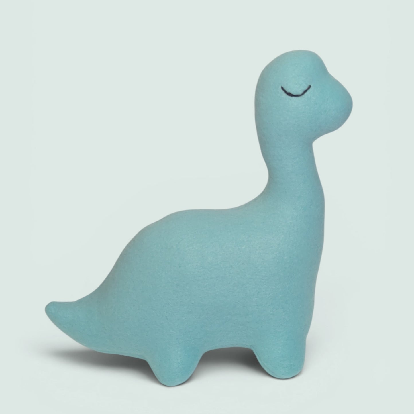 A light blue dinosaur-shaped plush toy with a soft fleece texture and a simple black stitched eye, shown against a neutral light gray background.