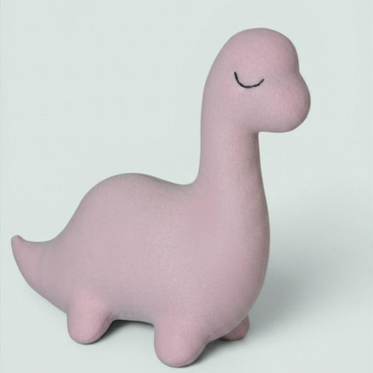 A light pink, dinosaur-shaped plush toy with a sleeping face, photographed on a solid light gray background.