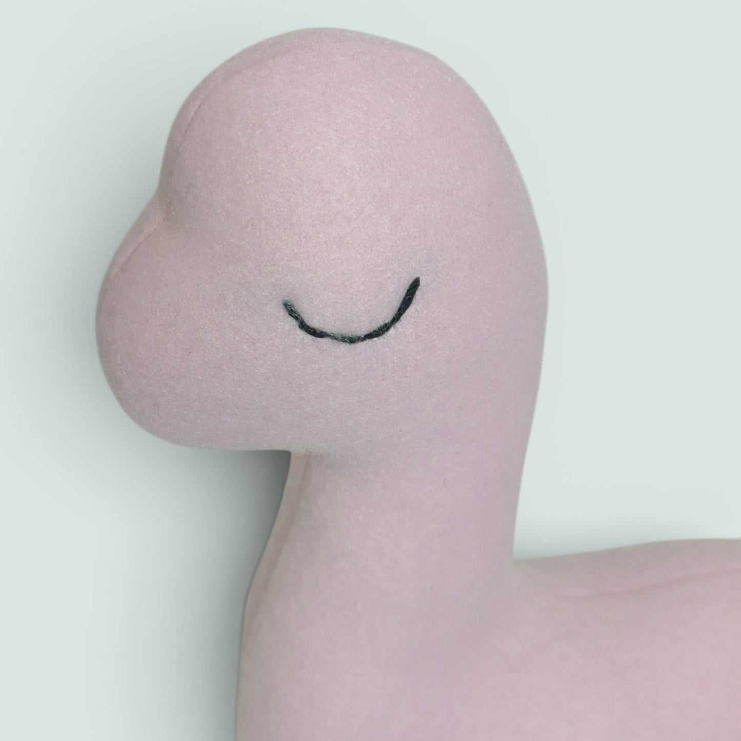 A pink plush dinosaur toy with an embroidered sleepy eye photographed close up of the face