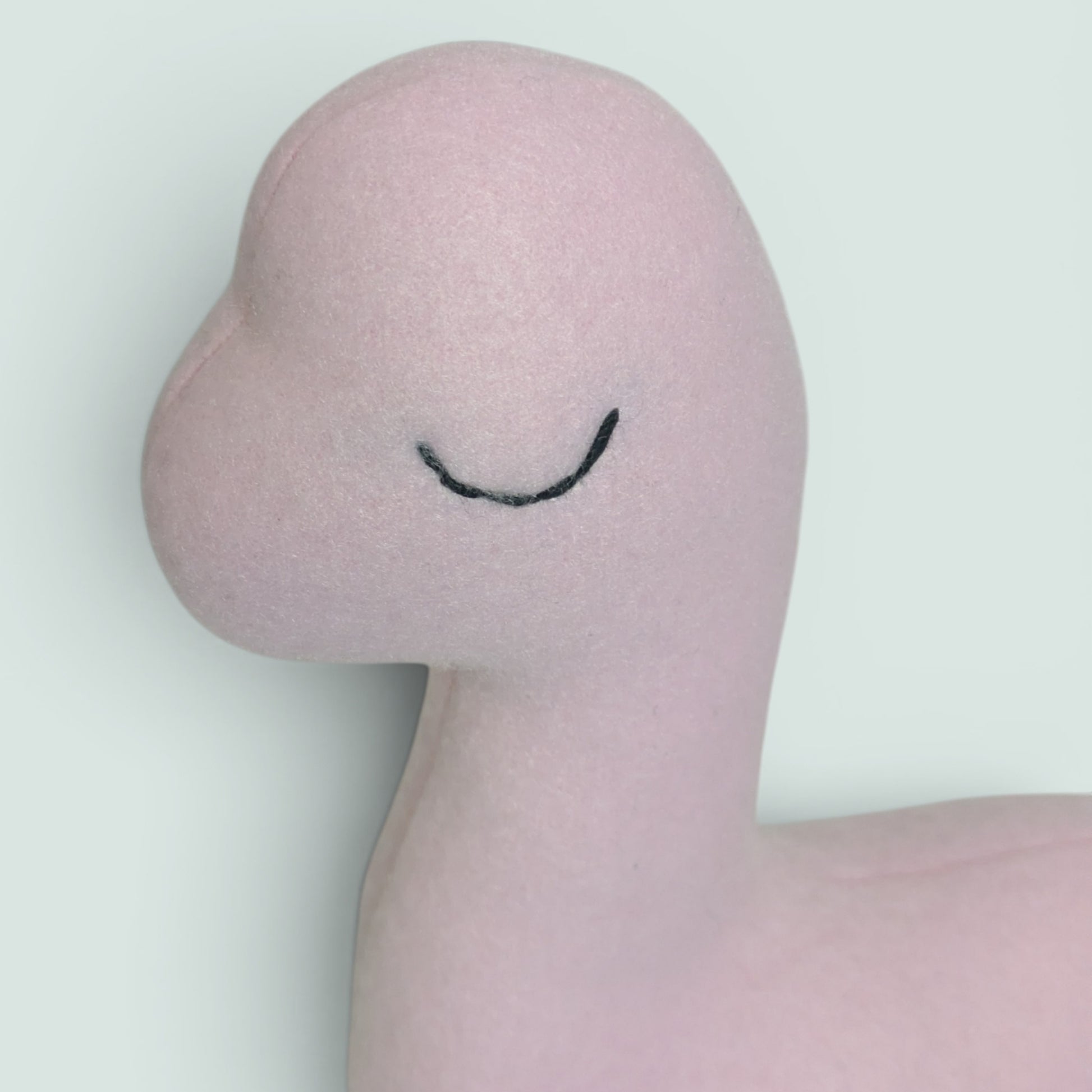 A pink plush dinosaur toy with an embroidered sleepy eye photographed close up of the face
