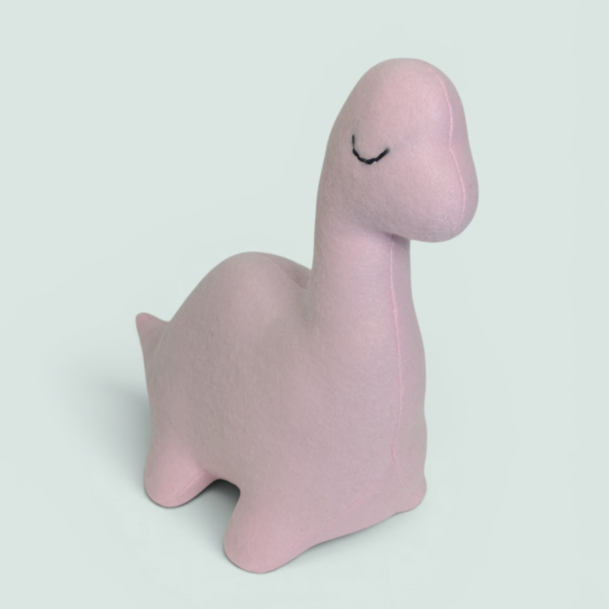 A light pink plush dinosaur toy with a simple black stitched closed-eye detail, shown on a solid pale gray background.
