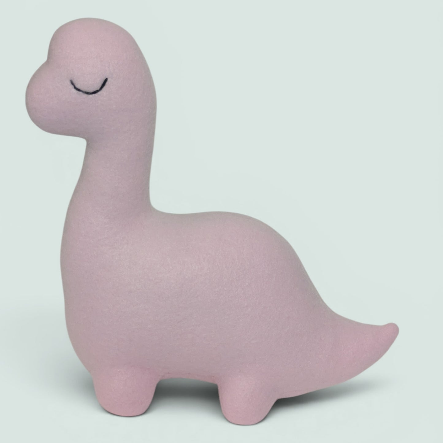 A soft, pale pink dinosaur-shaped plush with a long neck and closed embroidered eyes, shown against a plain light gray background.