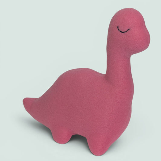 A pink fleece dinosaur toy with a long neck and a simple embroidered sleepy face, shown on a light gray background.
