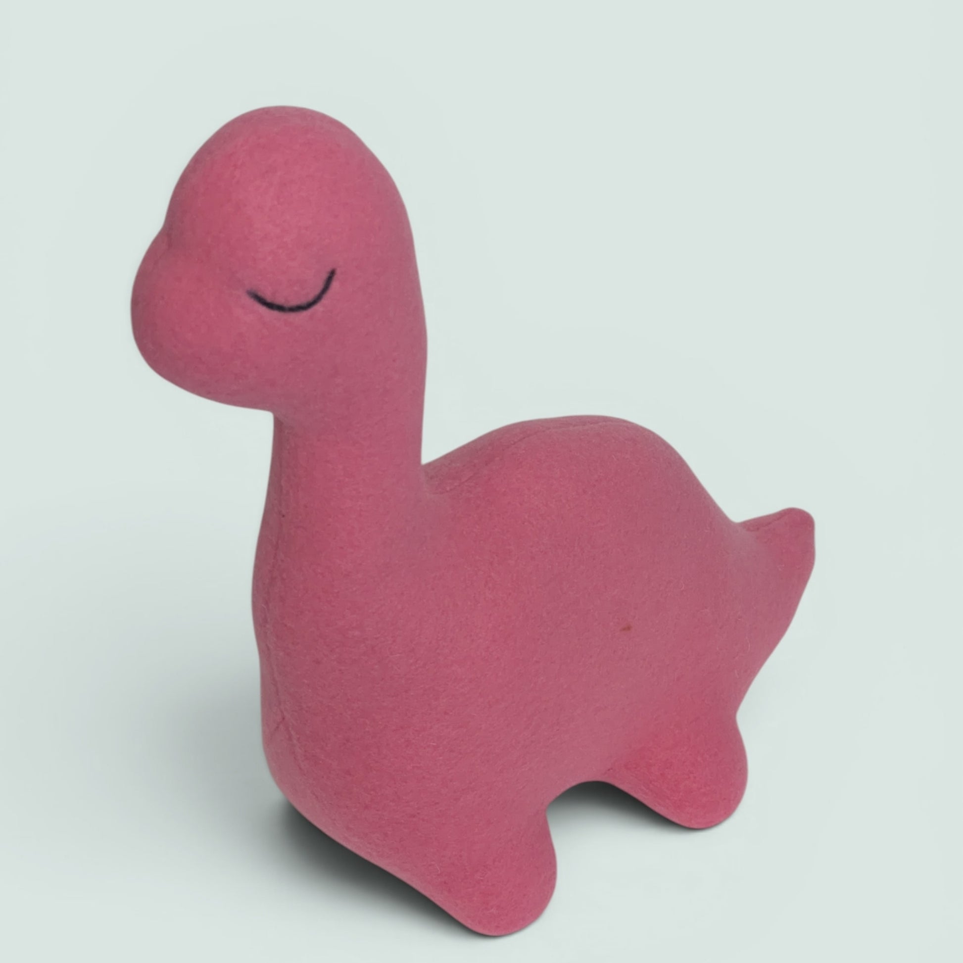 A pink plush dinosaur toy with a sleeping face, photographed on a light gray background.