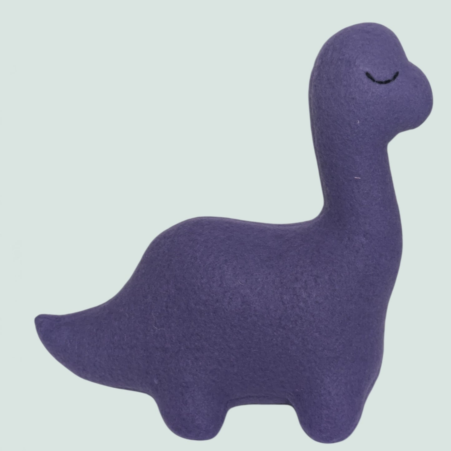 A purple fleece dinosaur toy with a long neck and closed embroidered eyes, shown against a solid pale gray-green background.