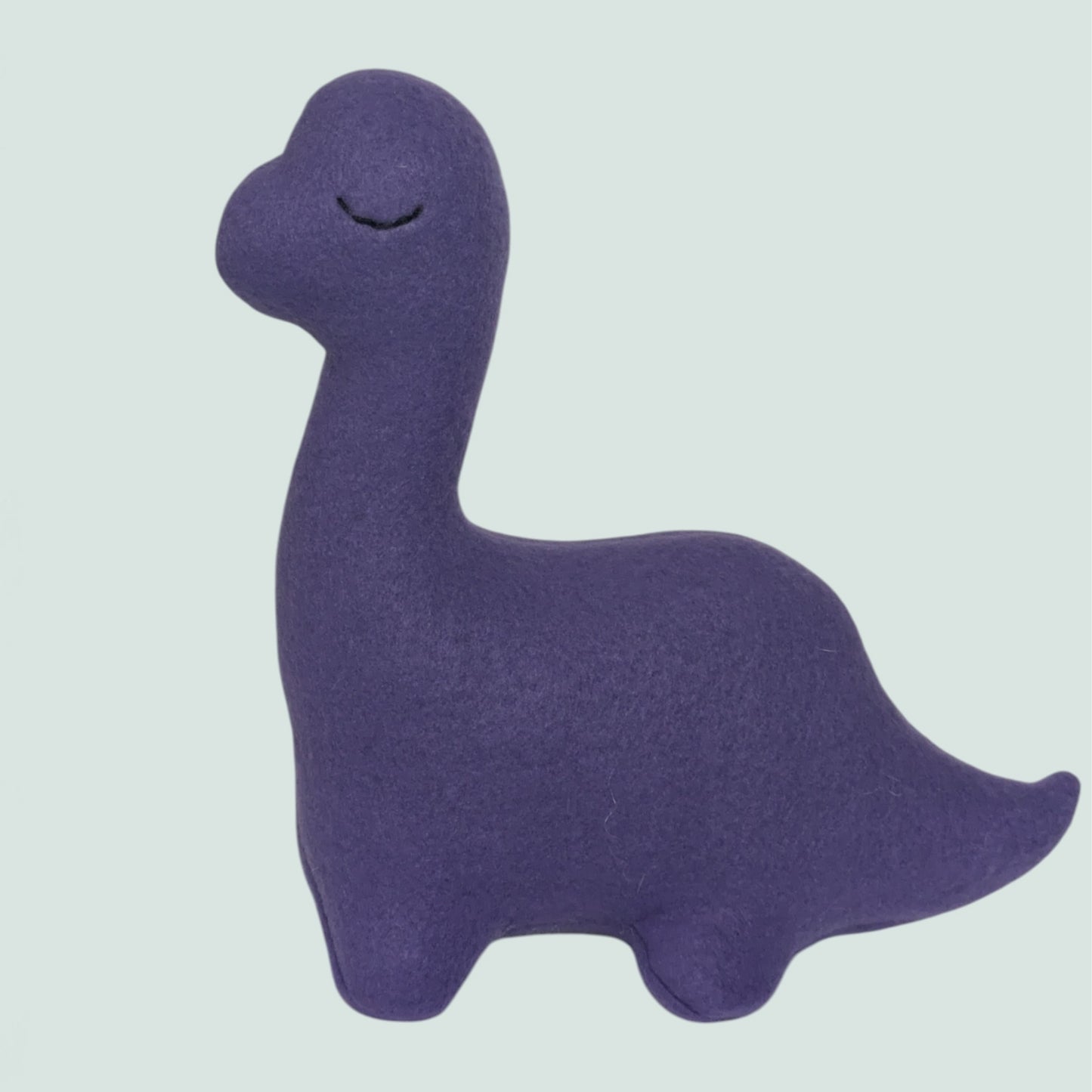 A purple fleece dinosaur toy with a long neck and stitched closed eyes, shown against a solid pale gray-green background.