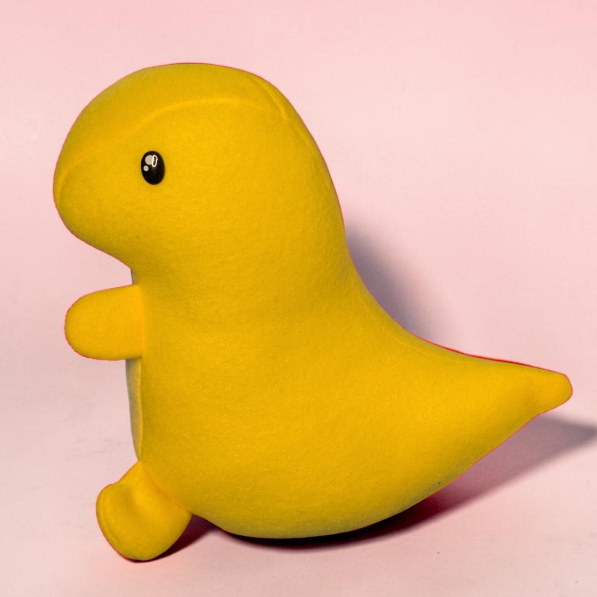 A bright yellow plush dinosaur toy with a small black eye, standing on a light pink background.
