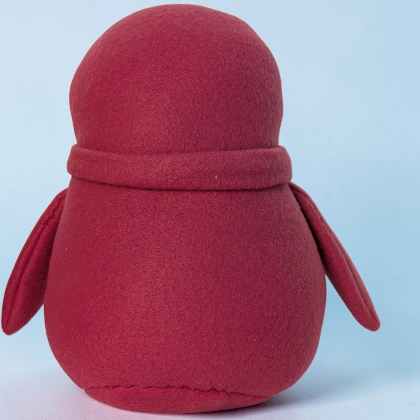 A small plush penguin toy made of fleece fabric, shown from the back against a light blue background.