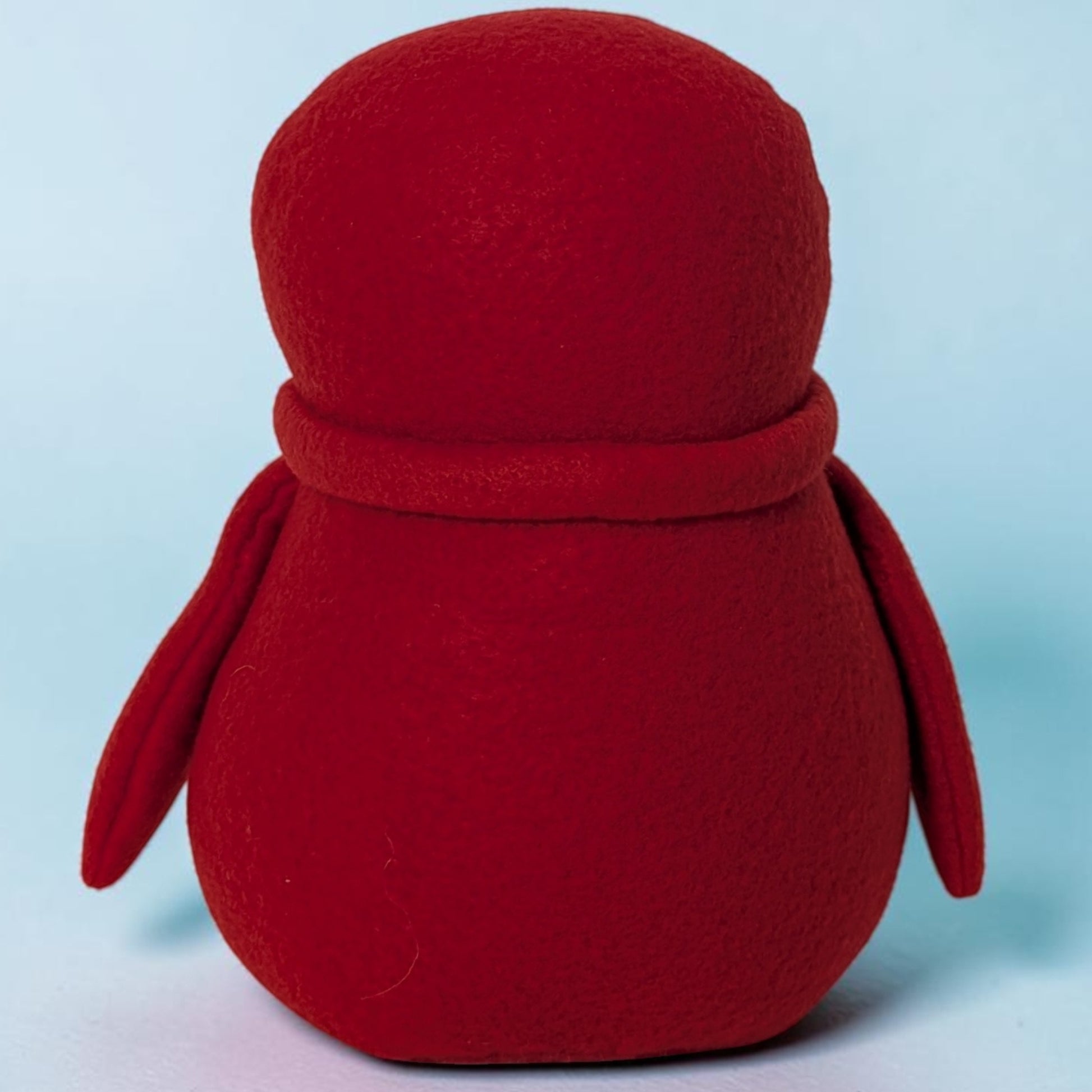 A red plush penguin toy with a soft felt texture, shown from the back against a light blue background.